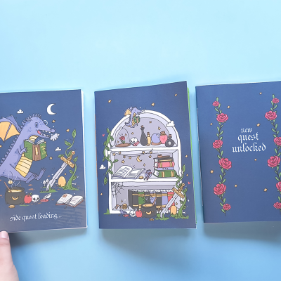 Três cadernos com capas azuis e desenhos de fantasia, incluindo dragão, poções e rosas.