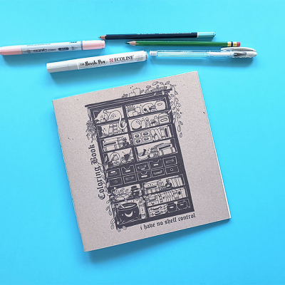 Caderno de colorir com canetas e lápis organizados sobre fundo azul.