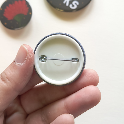 Botão redondo com alfinete visto por trás, segurado pela mão, com outros botões desfocados ao fundo