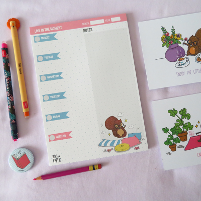 Bloco semanal, canetas coloridas, lápis e postais com desenhos de esquilos sobre fundo rosa.