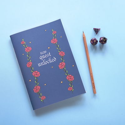 Caderno azul decorado com rosas, lápis de madeira e dados roxos sobre fundo azul