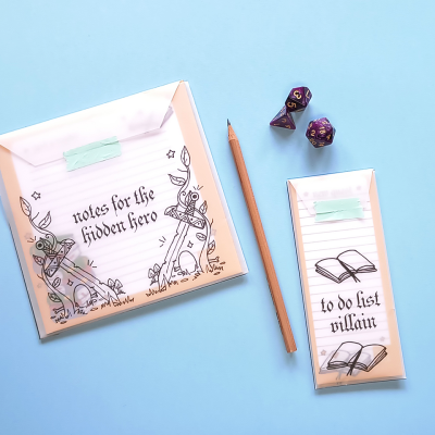 Dois blocos de notas com frases em inglês, lápis e dados sobre fundo azul claro