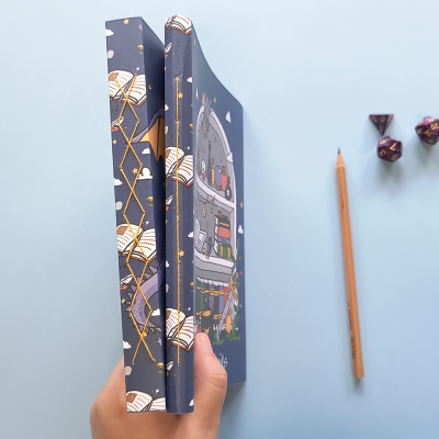 Livro de capa dura azul com ilustrações coloridas, lápis e dados políedricos