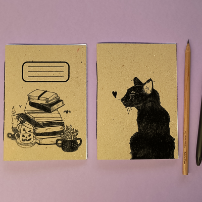 Dois cadernos com ilustrações em cartão reciclado, lápis e caneta sobre fundo lilás