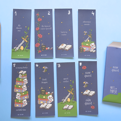 Oito marcadores de página coloridos com ilustrações e texto em inglês sobre fundo azul, com embalagem e lápis à lado