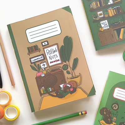 Cadernos ilustrados com desenhos de interiores e um urso, com vários objetos de papelaria ao redor.