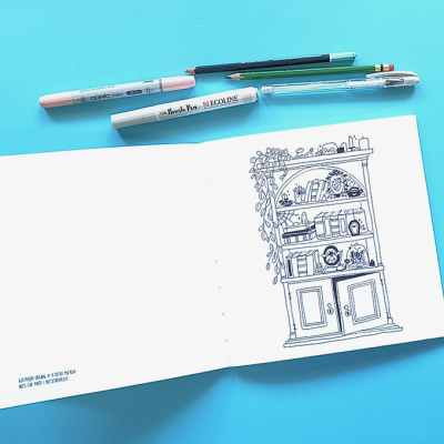 Livro de esboços aberto com desenho de estante ao lado de canetas sobre fundo azul