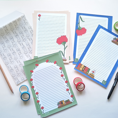 Folhas de papel decoradas com flores e livros, fitas adesivas coloridas e caneta em fundo branco