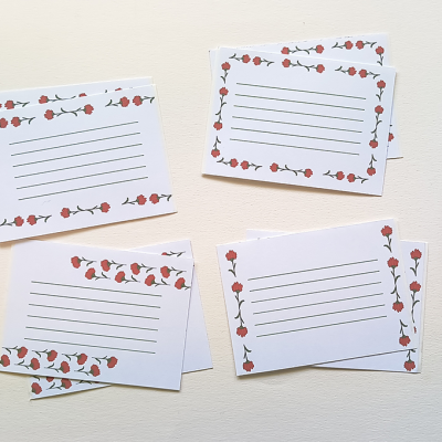 Cartões brancos com linhas e padrão floral vermelho, caneta preta, fita adesiva vermelha