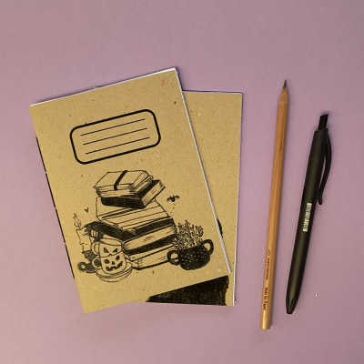 Cadernetas castanhas com ilustrações, lápis de madeira e caneta preta sobre superfície rosa