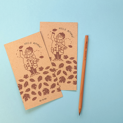 Dois cadernos castanhos com ilustração e lápis cor de madeira sobre fundo azul claro