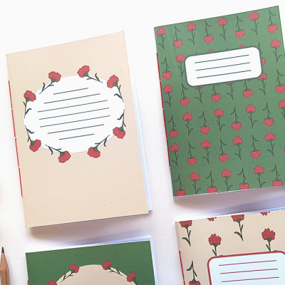 Quatro cadernos com capas florais em verde e bege, etiquetas brancas com linhas, lápis e fita adesiva em fundo branco