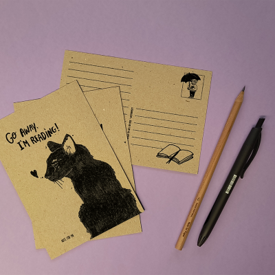 Três postais de papel reciclado com desenhos a preto, um lápis e uma caneta sobre fundo lilás