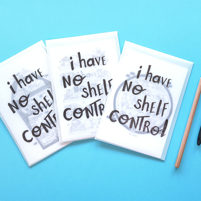 Três cadernos com capa branca e texto i have NO SHELF CONTROL, lápis e caneta sobre fundo azul