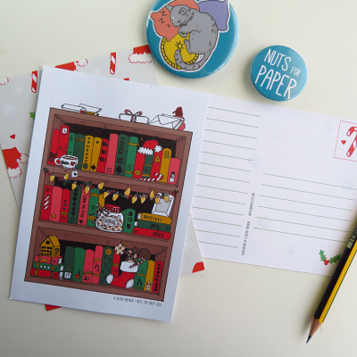 Cartão postal ilustrado com estante de livros e decoração de Natal, pins redondos azuis, lápis e envelope com padrão de bengalas vermelhas
