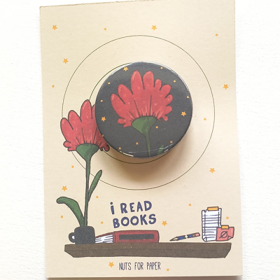 Fita adesiva decorativa com padrão de flor vermelha sobre fundo cinza, em cartão ilustrado com planta e livros.