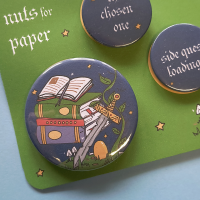 Três bottons redondos com desenhos e texto, sobre suporte verde com texto e estrelas