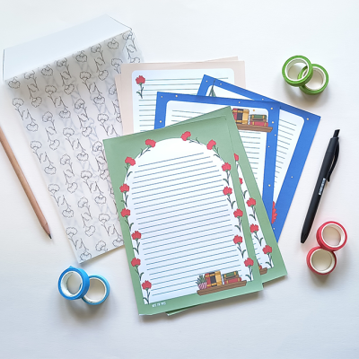Papel de carta com decoração de livros e rosas, lápis, caneta, fita adesiva colorida e envelope com padrão de gatos