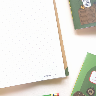 Página de caderno pontilhada, lápis verde e capa de caderno verde com ilustração musical