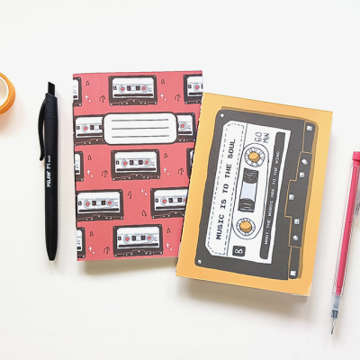 Dois cadernos decorados com cassetes, caneta preta, lápis mecânico vermelho e fita adesiva amarela