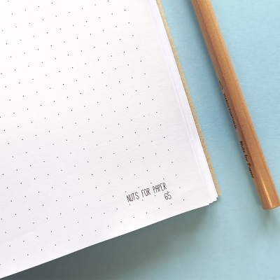 Caderno aberto com folhas de pontos e lápis num fundo azul claro