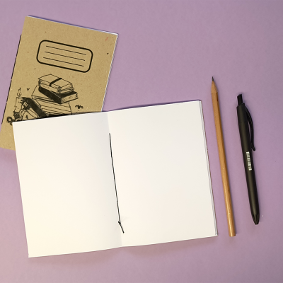 Caderno de capa castanha, caderno aberto, lápis de madeira e caneta preta sobre superfície lilás