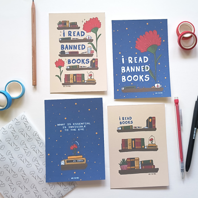 Quatro cadernos com frases sobre livros e ilustrações de flores vermelhas e estantes, com lápis, canetas e fitas adesivas ao redor.