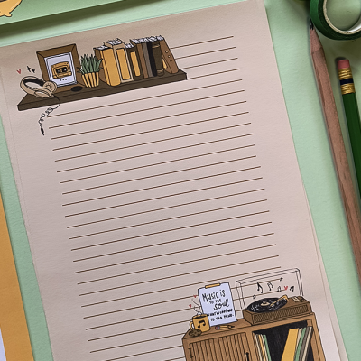 folha de papel com ilustrações de livros, planta e gira-discos, lápis e fita adesiva numa mesa verde