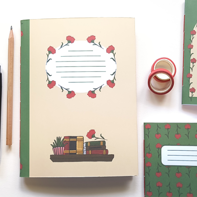 Cadernos decorados com livros e flores vermelhas ao lado de caneta, lápis e fita decorativa