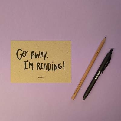 Post-it beige com texto manuscrito preto, lápis de madeira natural e esferográfica preta numa superfície lilás