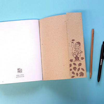 Caderno aberto com capa castanha e desenhos, lápis e caneta sobre fundo azul