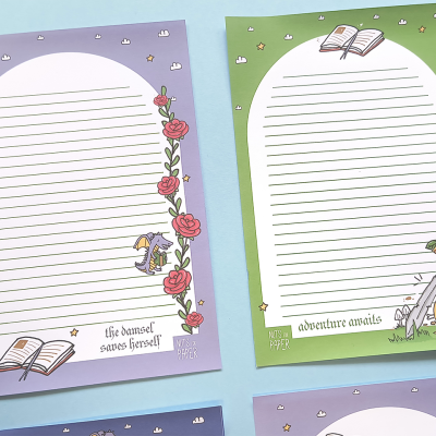 Folhas decorativas para escrita com temas de aventura e fantasia, em lilás e verde, com ilustrações de rosas, espada e livro.