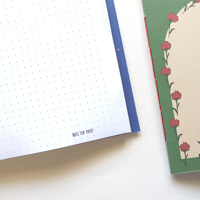 Dois cadernos, um aberto com páginas pontilhadas e texto, outro fechado com capa decorada com flores e plantas