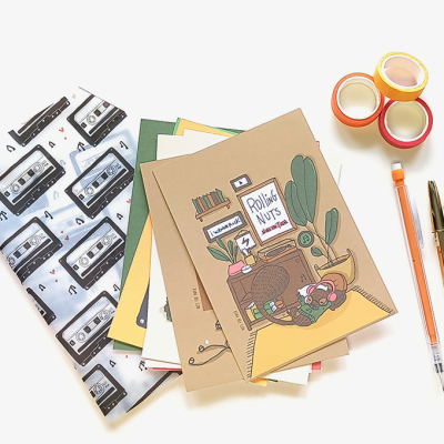 Conjunto de cadernos, canetas, fitas adesivas coloridas e saco com padrão de cassetes.