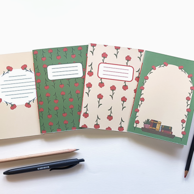 Quatro cadernos de capas florais com áreas para escrever, rodeados por canetas e lápis