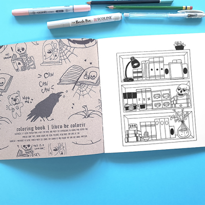 Livro de colorir aberto com ilustrações e canetas ao fundo