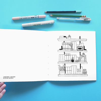 Livro aberto com desenho de estantes, canetas e lápis sobre fundo azul