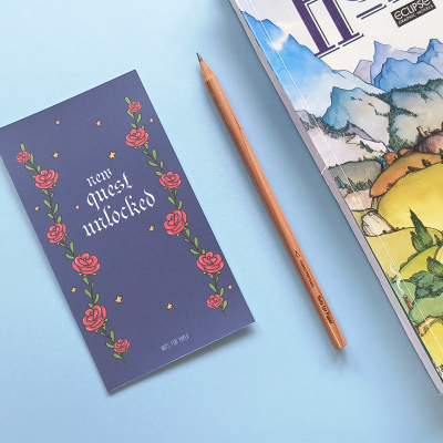 Cartão azul com texto 'item quest unlocked', lápis de madeira e canto de revista ilustrada