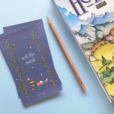 Bloco de notas azul escuro com ilustração e texto, lápis de madeira e livro colorido com paisagem