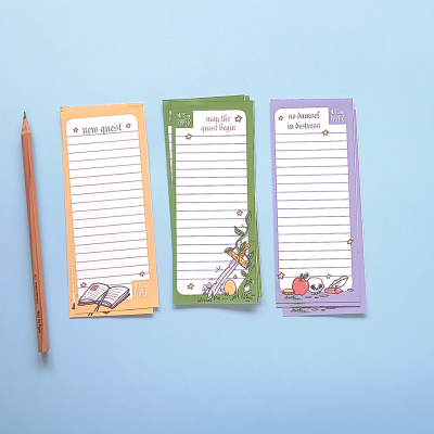 Três blocos de notas coloridos com linhas e textos em inglês, com desenhos decorativos e lápis de madeira sobre fundo azul