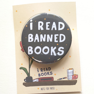 Pin preto com texto branco 'I READ BANNED BOOKS' em cartão ilustrado