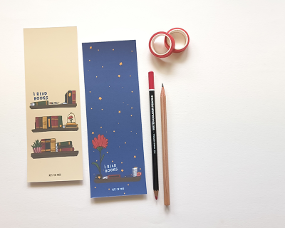 Marcadores de página com tema de livros, rolos de fita adesiva vermelha e lápis sobre mesa branca