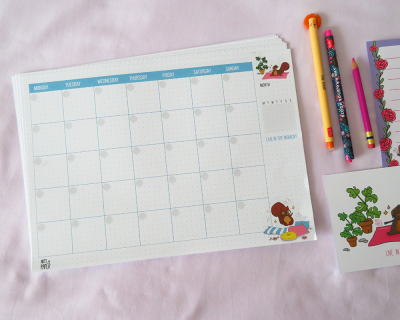 Calendário mensal em papel com ilustração de esquilo e canetas coloridas sobre tecido branco