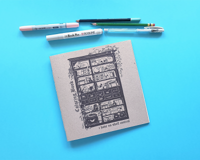 Caderno de colorir com canetas e lápis organizados sobre fundo azul.