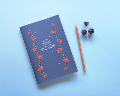 Caderno azul decorado com rosas, lápis de madeira e dados roxos sobre fundo azul