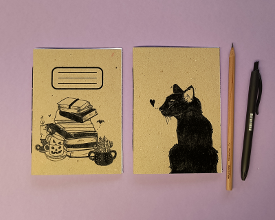 Dois cadernos com ilustrações em cartão reciclado, lápis e caneta sobre fundo lilás