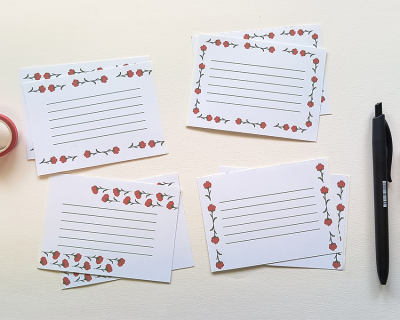 Cartões brancos com linhas e padrão floral vermelho, caneta preta, fita adesiva vermelha
