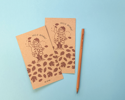 Dois cadernos castanhos com ilustração e lápis cor de madeira sobre fundo azul claro