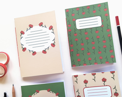 Quatro cadernos com capas florais em verde e bege, etiquetas brancas com linhas, lápis e fita adesiva em fundo branco