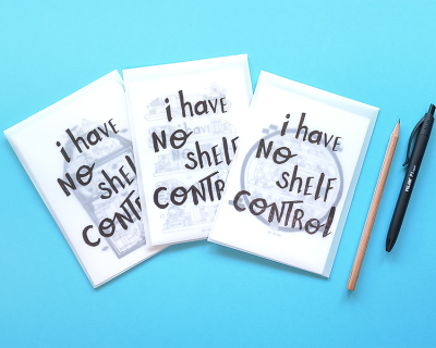 Três cadernos com capa branca e texto i have NO SHELF CONTROL, lápis e caneta sobre fundo azul